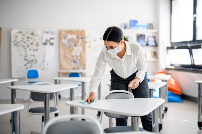 Teacher disinfecting classroom desks.